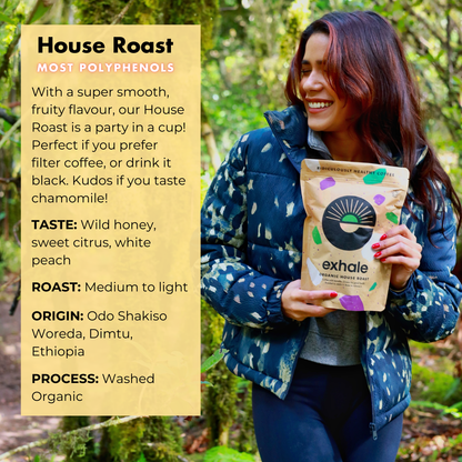 Organic house roast coffee by Exhale Healthy Coffee shown in a bag with a scoop and brewed coffee cup on a wooden table.
