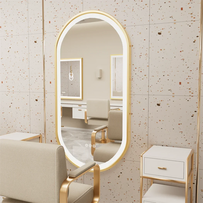 Large oval mirror with gold frame in a room with beige chairs and furniture.