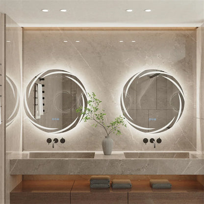 A modern bathroom interior with two large oval backlit mirrors mounted on a light stone wall above a double sink. The scene includes a vase with greenery, folded towels, and recessed ceiling lighting.