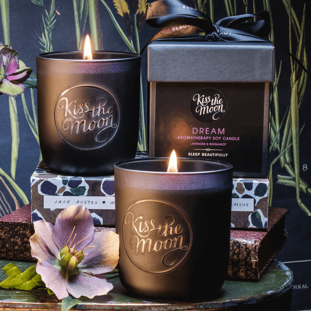 Aromatherapy soy candle by Kiss the Moon featuring lavender and bergamot scents, with a white jar and flickering flame.