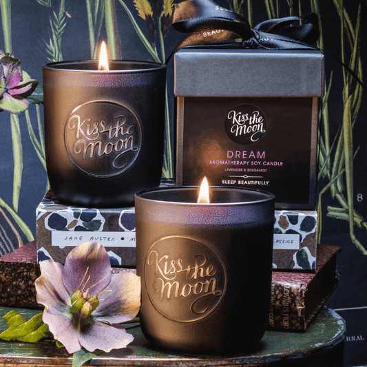 Aromatherapy soy candle by Kiss the Moon featuring lavender and bergamot scents, with a white jar and flickering flame.