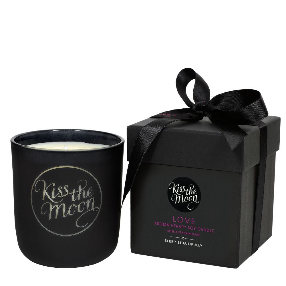 Aromatherapy soy candle by Kiss the Moon with a rose and frankincense scent, featuring a glass jar and a lit wick.