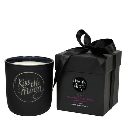 Aromatherapy soy candle by Kiss the Moon with a rose and frankincense scent, featuring a glass jar and a lit wick.