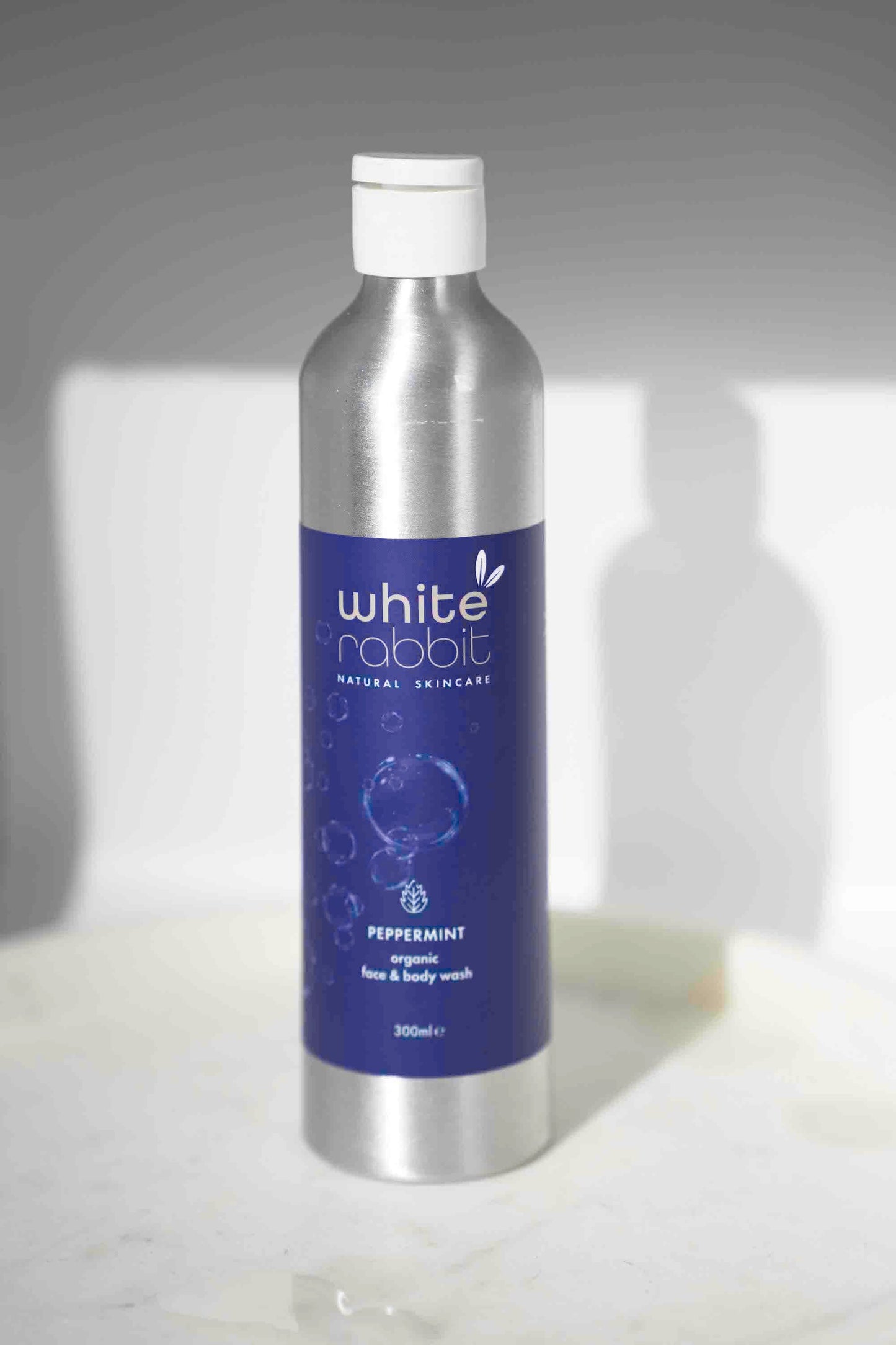 White Rabbit Organic Peppermint Face and Body Wash bottle with white and green label, highlighting natural ingredients and refreshing scent.